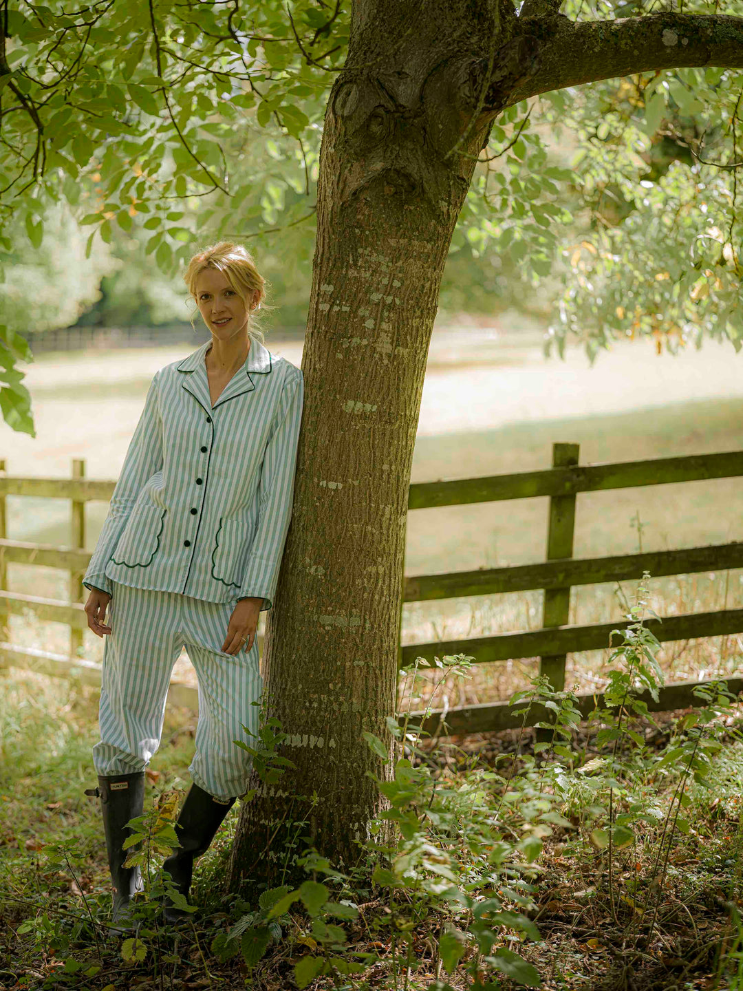 Woman wearing green striped brushed cotton pyjamas with scalloped pockets and hems from Siân Esther, made in Portugal using Better Cotton Initiative cotton, combining comfort and timeless elegance. 1