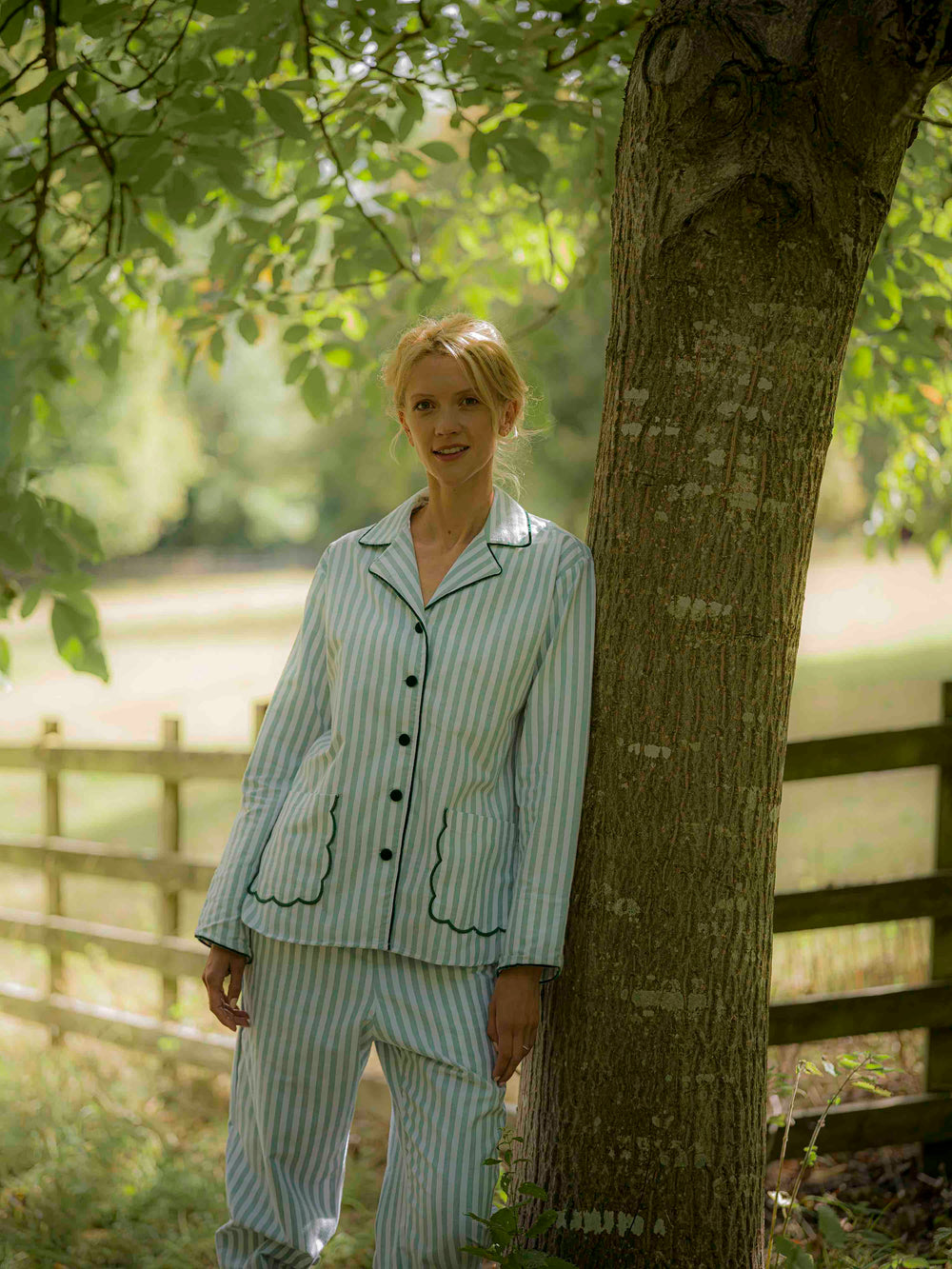 Woman wearing green striped brushed cotton pyjamas with scalloped pockets and hems from Siân Esther, made in Portugal using Better Cotton Initiative cotton, combining comfort and timeless elegance